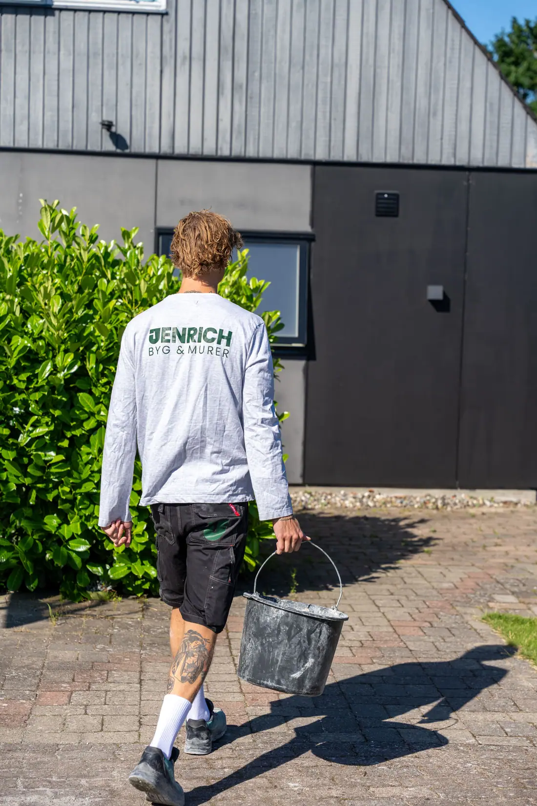 Murer fra Jenrich Byg & Murer set bagfra med firmalogo på arbejdstøjet foran en facade